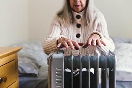 A retired senior woman in her 70s sits at home inside her cold house in winter.