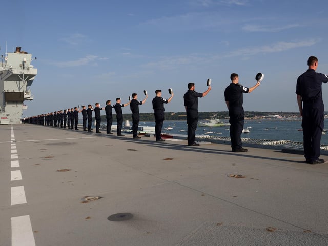 Pictured members of the ship's company lining the upper deck with HMS Tyne in the background.