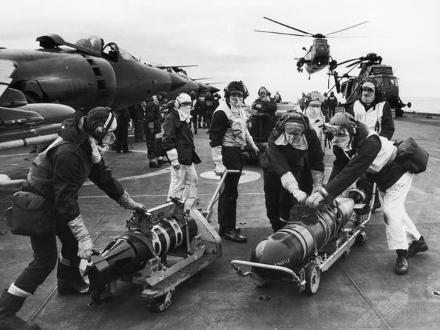 Armourers moving torpedoes on the flight deck of HMS Hermes during the Falklands conflict, May 1982. The torpedoes are to re-arm Sea King helicopters to counter the threat from Argentinian submarines.