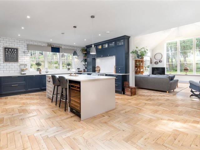 The kitchen area is fitted with sleek, tall cabinets, a large central island with breakfast bar, and marble surfaces. Integrated appliances include an electric range cooker, fridge freezer, dishwasher and wine cooler.