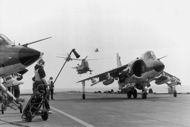 A Sea Harrier jump jet on the flight deck of HMS Hermes heading to the Falklands after the Argentinian invasion of the islands, April 1982. A Sea King helicopter hovers in the background. (Photo by Martin Cleaver/Pool/Getty Images)