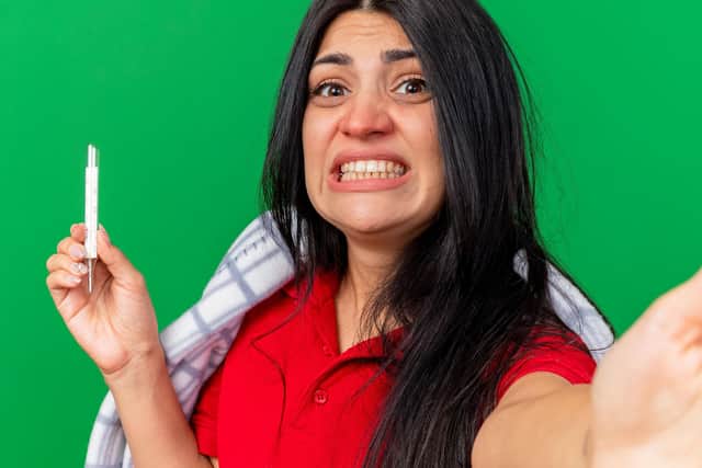 A concerned woman holds a thermometer while clenching her jaw.