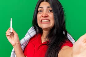 A concerned woman holds a thermometer while clenching her jaw.