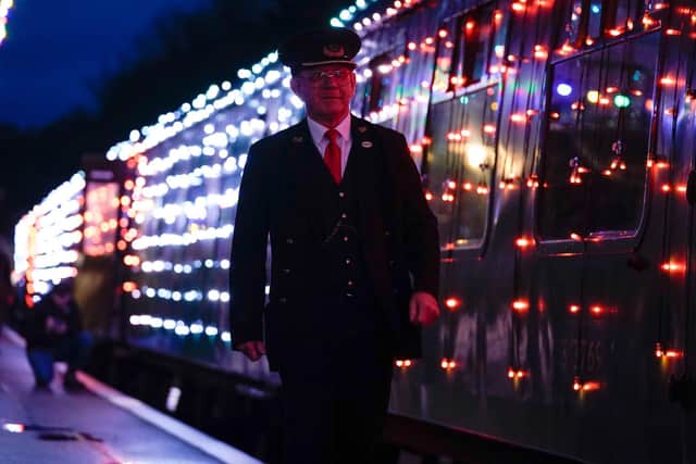 A guard walks past a Steam Illuminations train, a light show on and in a steam train, consisting of thousands of fully controllable colour mixing LED lights, as it stops at Alresford station on the Watercress Line in Hampshire, which forms part of their Christmas programme of events. Picture date: Friday November 12, 2021. PA Photo. Photo credit should read: Andrew Matthews/PA Wire
                                   