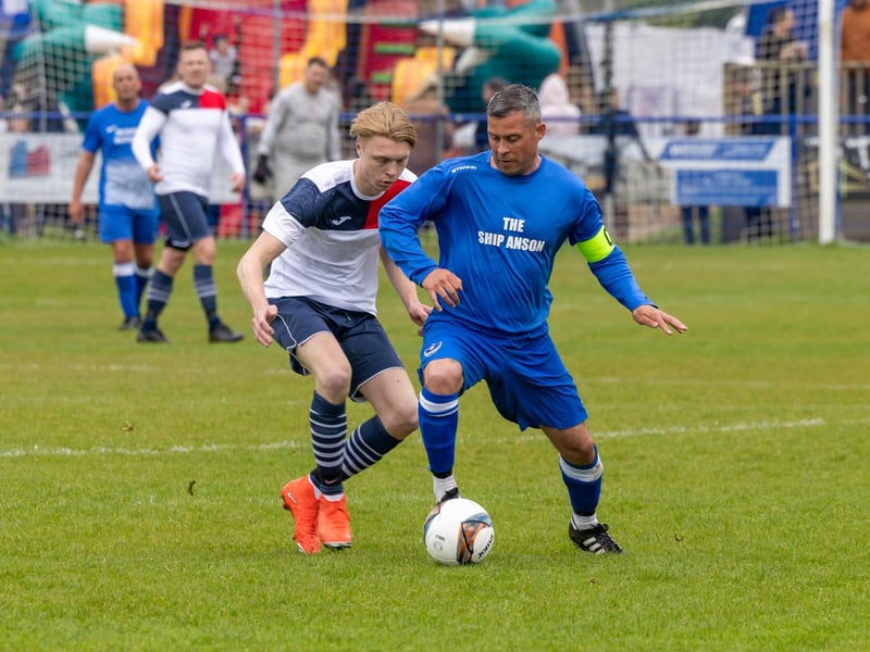 The players compete on the pitch while children enjoy the bouncy castle in the background.