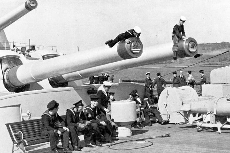 The ship's company of the battleship HMS Vanguard. The two men on the barrels of A turret are polishing the muzzle and the tampions that can be seen inserted into the barrels.