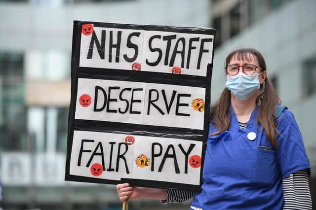 A nurse wearing scrubs holds a placard calling for a pay rise for NHS nursing staff. Credit: Getty Images