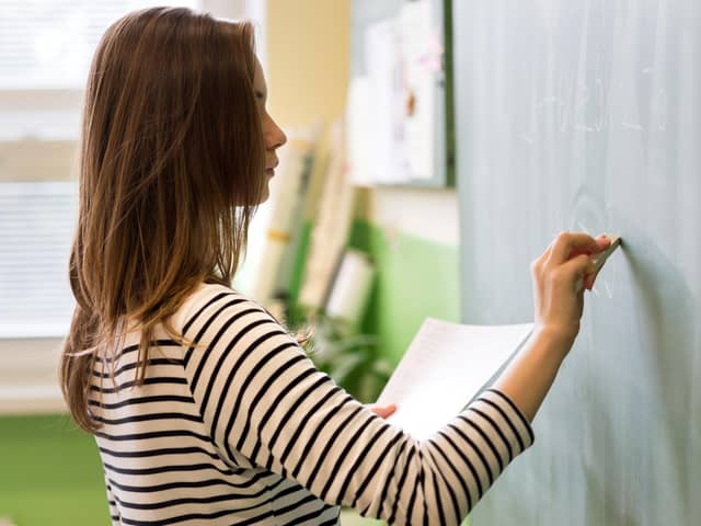 Young female teacher or a student writing math formula on blackboard in classroom.