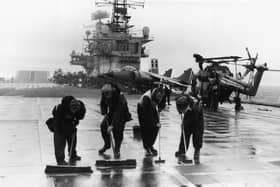 Four men scrubbing the flight deck on HMS Hermes during the Falklands conflict, May 1982. (Photo by Martin Cleaver/Pool/Getty Images)