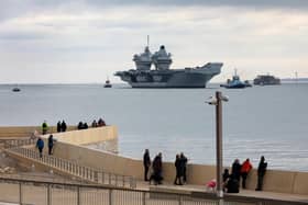 HMS Queen Elizabeth approaches the newly reopened walkway on the sea defences at Long Curtain Moat