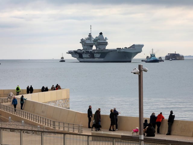 HMS Queen Elizabeth approaches the newly reopened walkway on the sea defences at Long Curtain Moat