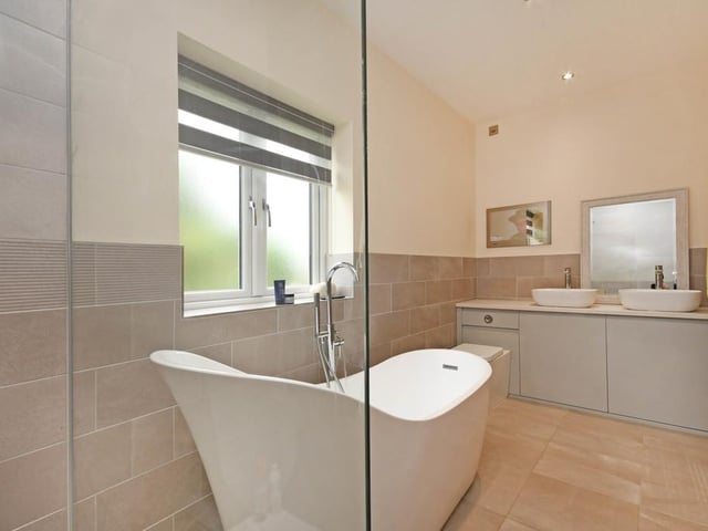 A contemporary en-suite bathroom with a walk-in digitally operated shower, free-standing bath, concealed cistern W/C and dual basin vanity unit.