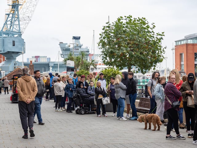HMS Queen Elizabeth enters Portsmouth harbour behind queues of people waiting to enter the new Pompey Store in Gunwharf Quays. Picture: Mike Cooter (011124)