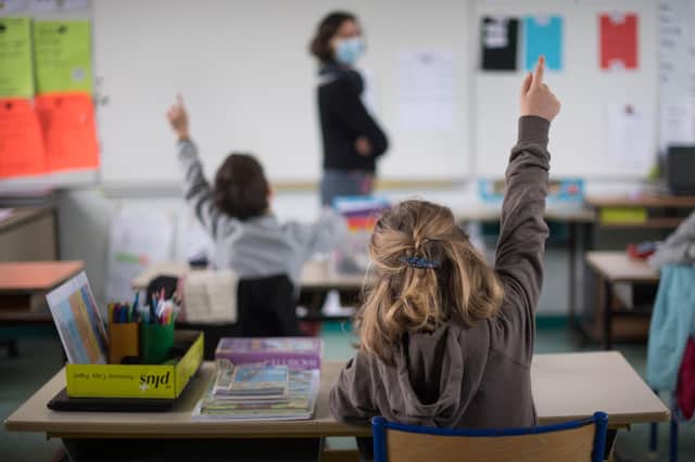 Pupils raise their hands as they speak with a teacher wearing a protective face. Picture: LOIC VENANCE/AFP via Getty Images