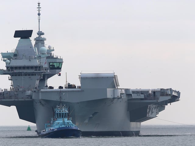 HMS Queen Elizabeth approaches the newly reopened walkway on the sea defences at Long Curtain Moat, as she returns to Portsmouth Naval Base