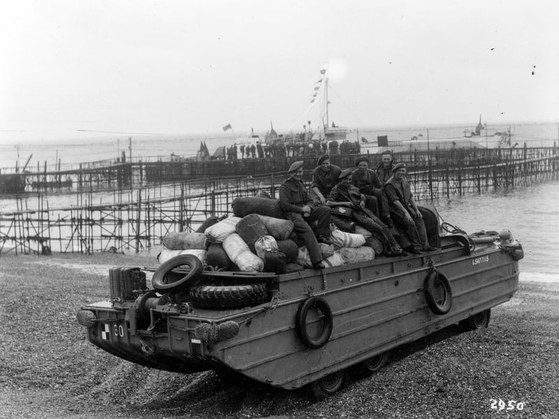 An amphibious DUKW, known as a duck, on Southsea beach with a temporary pier structure in the background