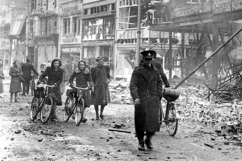 A close up of the girls pushing their cycles through a bombed out Commercial Road. But who are they? Mcllroy's Store pictured behind.