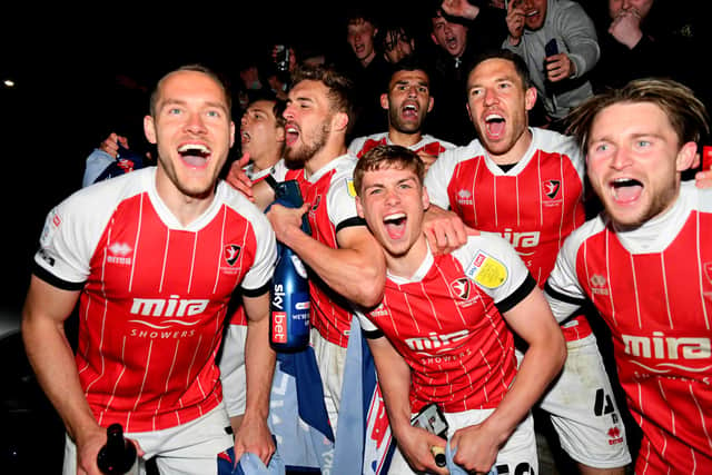 CHELTENHAM, ENGLAND - APRIL 27: Players and fans of Cheltenham Town celebrate their side's victory outside the ground as they gain promotion to the Sky Bet League One after the Sky Bet League Two match between Cheltenham Town and Carlisle United at The Jonny-Rocks Stadium on April 27, 2021 in Cheltenham, England. Sporting stadiums around the UK remain under strict restrictions due to the Coronavirus Pandemic as Government social distancing laws prohibit fans inside venues resulting in games being played behind closed doors.  (Photo by Dan Mullan/Getty Images)