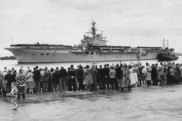 Officers and crew line the flight deck of the Royal Navy Centaur-class light fleet aircraft carrier HMS Bulwark as she is waved off by family and holidaymakers on the quayside for patrol in the Mediterranean on 7 July 1956 Portsmouth, United Kingdom.  (Photo by George W. Hales/Fox Photos/Hulton Archive/Getty Images).