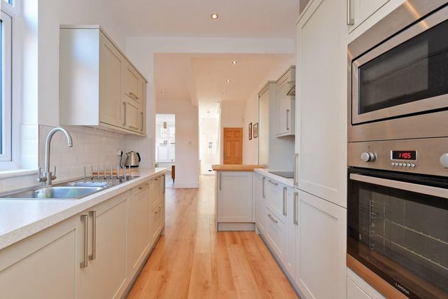The kitchen has a range of pale grey floor and wall units, white marble effect work surfaces and integrated appliances including an electric hob, extractor, dishwasher, fridge freezer, microwave and oven. There is a breakfast bar with a solid wood worktop.