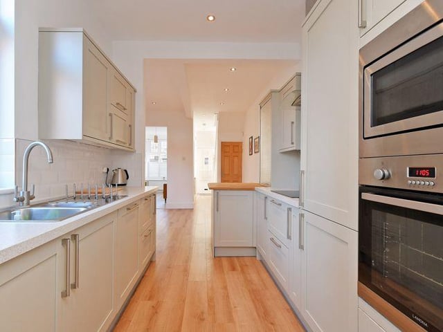 The kitchen has a range of pale grey floor and wall units, white marble effect work surfaces and integrated appliances including an electric hob, extractor, dishwasher, fridge freezer, microwave and oven. There is a breakfast bar with a solid wood worktop.