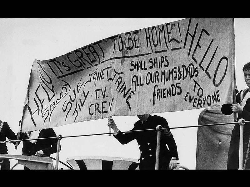 Sailors aboard HMS Intrepid unfurl their own special banner from the flight deck.1982