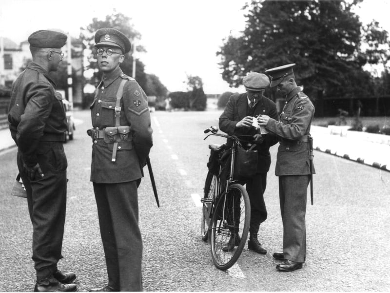 Military policemen checking the identity papers of a male civilian cyclist, 17.8.1943. This was the first day that special additional identity documents were required for anyone who wanted to go to the Southsea seafront area. These security measures were put in place in anticipation of preparations for D-Day. The location is the southern end of Festing Road, and what is now the Natural History Museum at Cumberland House can be seen in the left background.