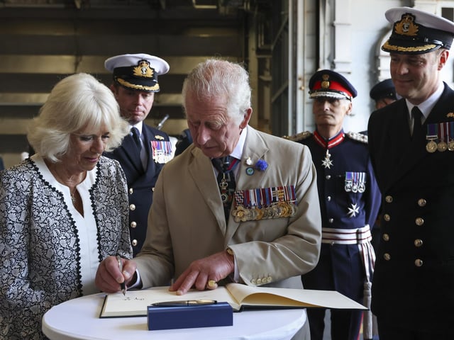 The then The Duchess of Cornwall and The Prince of Wales sign the HMS Queen Elizabeth visitor's book during a visit in July 2022 at a unique ‘garden party’ in her hangar for hundreds of veterans of the Falklands conflict.