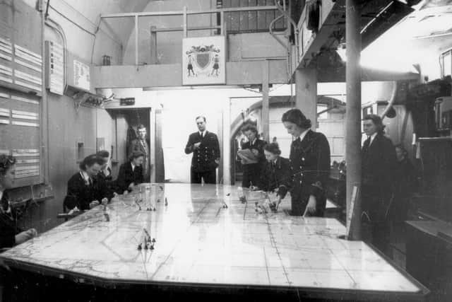 The plotting room in the underground headquarters at Fort Southwick, 1944. Tunnels beneath the fort housed the Combined Operations Underground HQ which played an important command and communications role in the D-Day Landings. In the plotting room, Wrens (members of the Women's Royal Naval Service) plotted naval movements in the English Channel on a map. In the background can be seen the unofficial coat of arms of the plotting room. The coat of arms was designed by Wren 3rd Officer Dorothy C.P. Ward who worked on the main plot, and is now on display at The D-Day Story. 