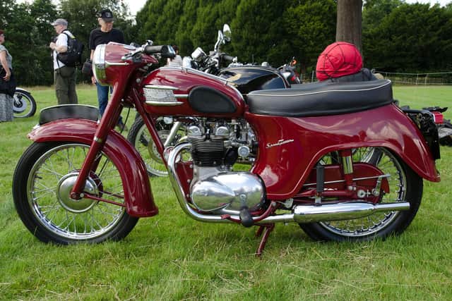 Liz's husband's bike is the same model as the one pictured but in a chrome and grey colour and not red. Triumph 5TA Speed Twin (1960). 

Credit: https://commons.wikimedia.org/wiki/Category:Photographs_by_Steve_Glover
SG2012, CC BY 2.0 , via Wikimedia Commons