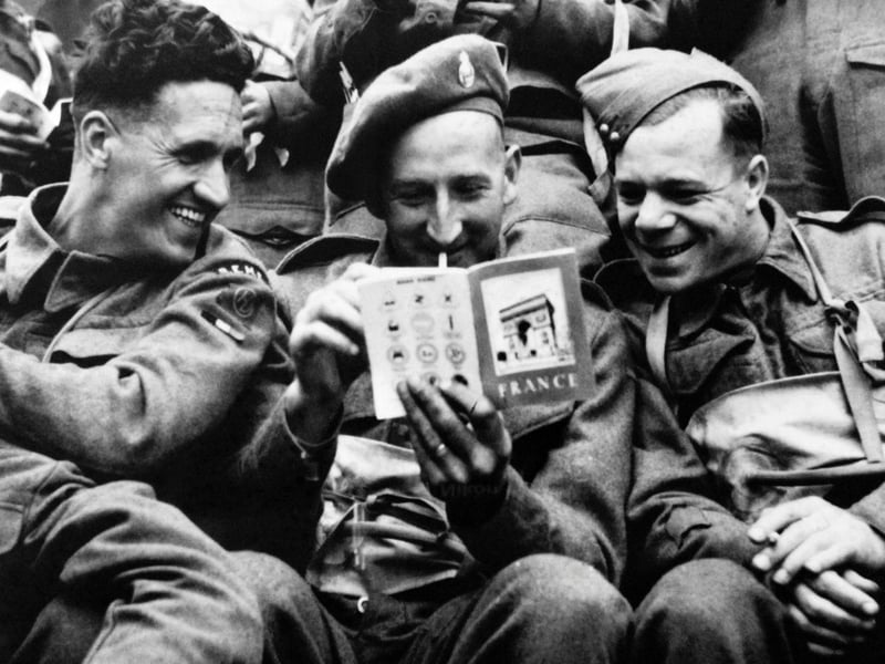 June 1944 of British soldiers joking as they read a tourist guide about France aboard a landing craft while Allied forces storm the Normandy beaches on D-Day. (Photo credit should read -/AFP/Getty Images)