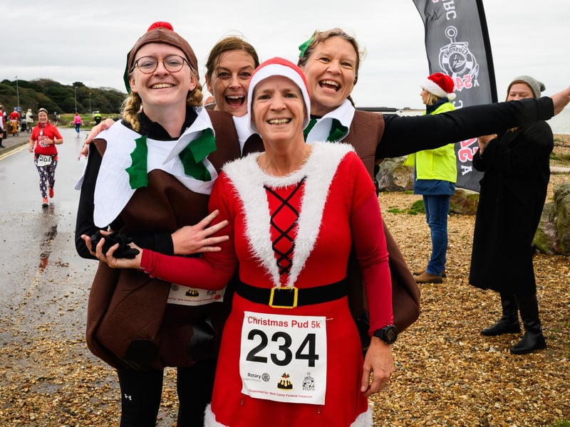 Four festive runners celebrate at the finish line of the Christmas Pud 5k, Stokes Bay, Gosport.