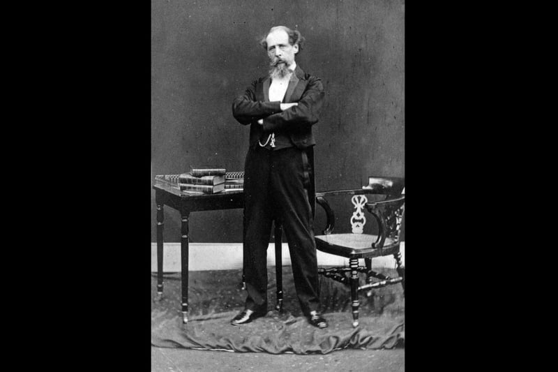circa 1868:  Charles Dickens (1812 - 1870) English novelist in later life dramatically posed standing in front of a table covered in books.  (Photo by Hulton Archive/Getty Images)