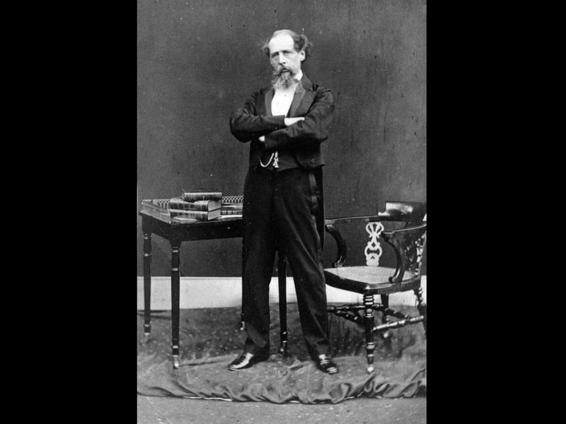 circa 1868: Charles Dickens (1812 - 1870) English novelist in later life dramatically posed standing in front of a table covered in books. (Photo by Hulton Archive/Getty Images)