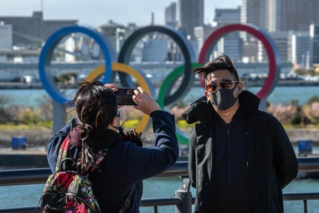 A man wearing a face mask has his photograph taken in front of the Olympic Rings in Odaiba, Tokyo, Japan. Covid-19 cases continue to grow and concerns mount over the possibility that the epidemic will force the postponement or even cancellation of the Tokyo Olympics. Photo by Carl Court/Getty Images.