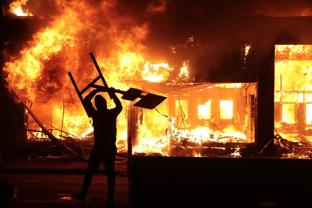 A man holds up a sign near a burning building during protests sparked by the death of George Floyd in Minneapolis, Minnesota. Photo by Scott Olson/Getty Images.