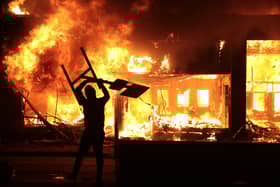 A man holds up a sign near a burning building during protests sparked by the death of George Floyd in Minneapolis, Minnesota. Photo by Scott Olson/Getty Images.