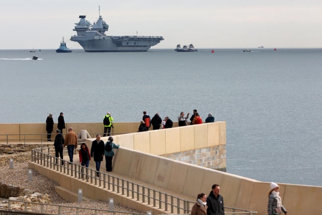 HMS Queen Elizabeth approaches the newly reopened walkway on the sea defences at Long Curtain Moat, as she returns to Portsmouth Naval Base