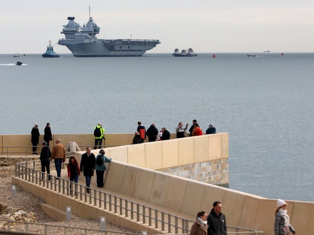 HMS Queen Elizabeth approaches the newly reopened walkway on the sea defences at Long Curtain Moat, as she returns to Portsmouth Naval Base