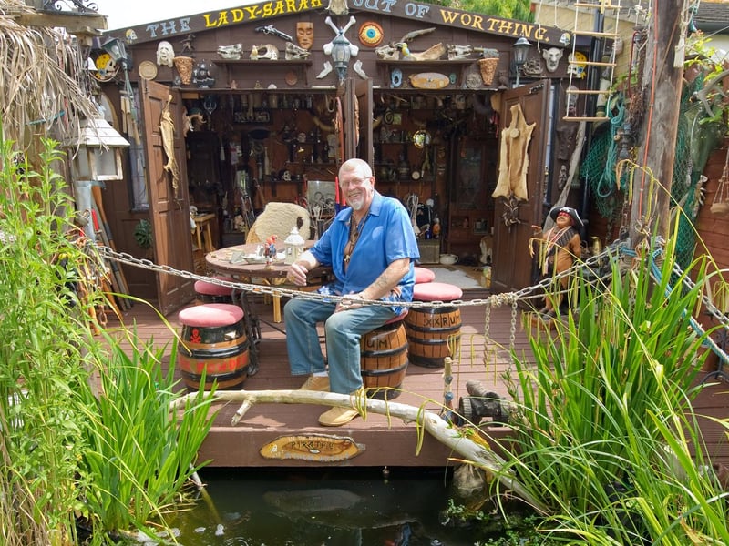 Shed of the Year 2010 - The Lady Sarah Out of Worthing - built by Reg Miller
My shed is a purpose built pirate's cabin built to look like the poop deck of a pirate ship moored at a Caribbean dock, complete with fully stocked koi carp pond and aviary - for those long hungry voyages! The inside of the shed is equipped with a full range of piratannical ephemera, including skulls, crossed bones (courtesy of a friendly butcher) and a dead man's chest. Outside the shed there is plenty of space for pirate roistering and carousing amongst the tropical plants and under the palm thatched lean-to. The front of the shed opens completely to make the most of the evening sun and provides a suitable location for card playing, rum drinking and bad behaviour of every kind. The large number of empty rum bottles doubling as candle sticks provides evidence of this.