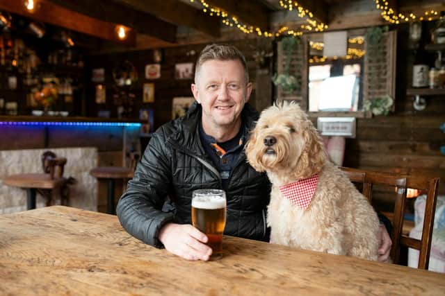John Simmons with dog Bertie at his pub shed called The Dog & Ball in Horndean, Hampshire.  An incredible back garden boozer made entirely from recycled materials has been crowned Britain's best Pub Shed of the Year.  See SWNS story SWMRshed.  John Simmons, spent more than a year constructing the amazing DIY man-cave in his garden in Portsmouth, Hamps.   It features its own dart board, wooden décor, countryside-pub style seating, a roof covered in fairy lights and even its own outdoor beer garden and decking area.   He built the miniature pub- called The Dog & Ball - from as much reclaimed material he could find from salvage yards and a Facebook page for pub shed enthusiasts.   John has now beat off more than a thousand entries to be named the owner of Britain's best Pub Shed 2022. :John Simmons, 50, of Portsmouth, has been crowned the owner of Britain's best pub shed. Picture: SWNS.