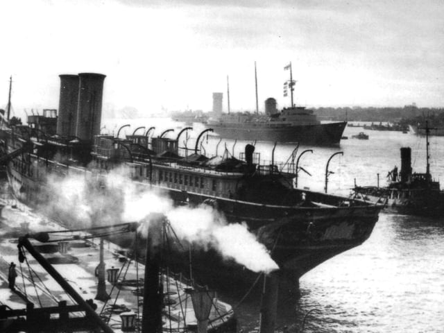 Stripped of her finery and masts, the Victoria and Albert III tied up alongside the South Railway Jetty is passed by her successor HMY Britannia.