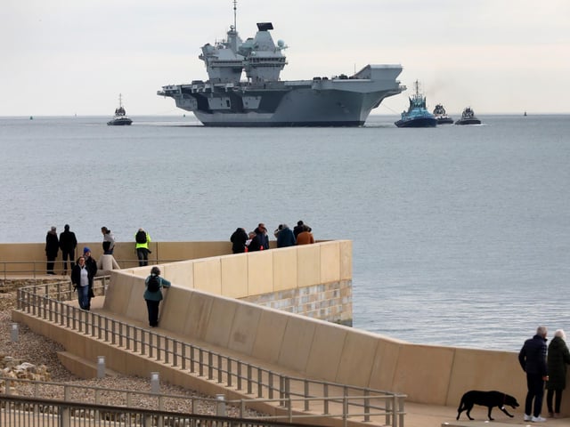 HMS Queen Elizabeth approaches the newly reopened walkway on the sea defences at Long Curtain Moat, as she returns to Portsmouth Naval Base.