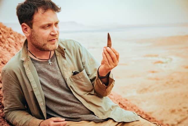 Nizar Ibrahim in the Sahara Desert holding a Spinosaurus tooth.