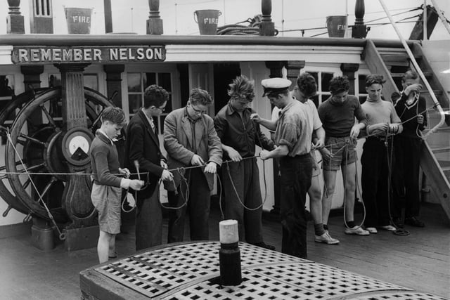 6th July 1954:  Schoolboys from Hither Green Secondary School in Lewisham, London, receiving a lesson in knot tying from John Veale, an instructor aboard the 'Foudroyant' at Portsmouth. The boys are taking part in a course arranged by the London County Council.  (Photo by Meager/Fox Photos/Getty Images)