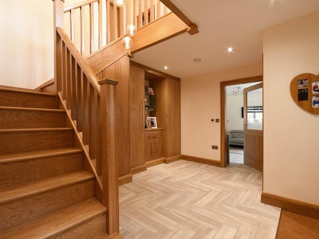 The entrance hallway has tiled flooring in a herringbone style, benefiting from under-tile heating that runs throughout the open-plan ground floor living space. There is a "beautiful, imposing" solid oak staircase, built-in oak finished storage cupboards and a downstairs W/C.