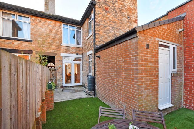 To the rear is an enclosed courtyard garden with a flagged seating terrace and a lawn laid with artificial grass.