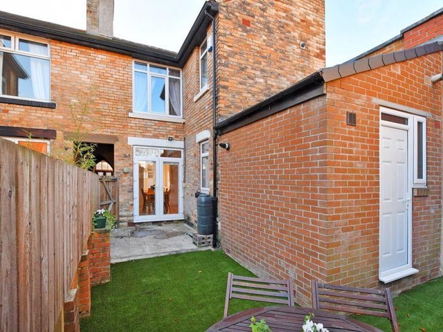 To the rear is an enclosed courtyard garden with a flagged seating terrace and a lawn laid with artificial grass.