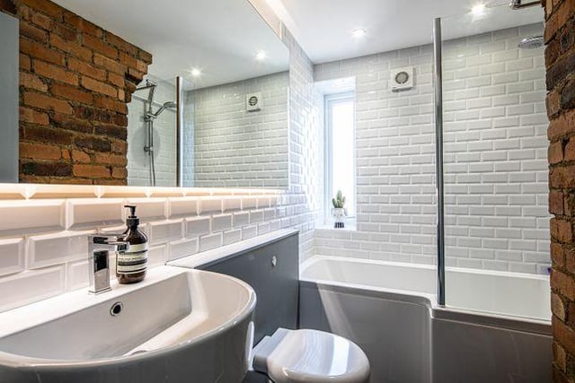 The modern bathroom has subway tiles and exposed brick.