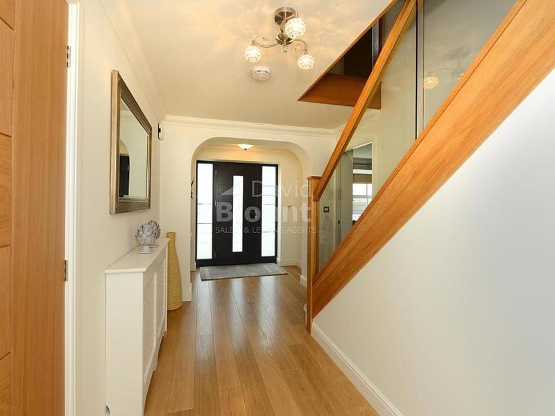 You are greeted by this entrance hall when you step through the front door. It features wooden veneer flooring and a glass balustrade staircase.